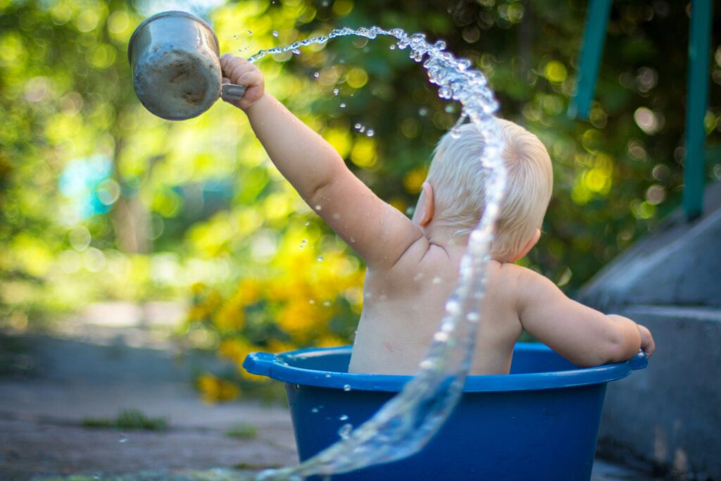 Baby sitting in blue bucket splashing water over their head